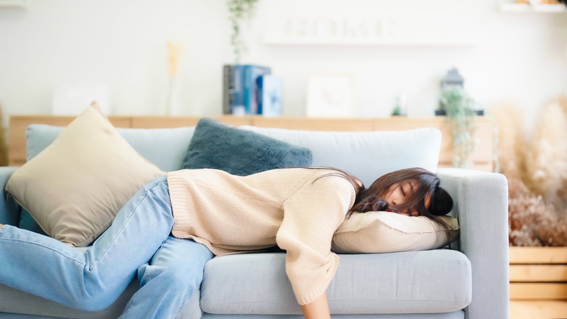 Asian woman resting at home on couch, feeling exhausted after work, lacking energy, or overworked, too tired, and lacking motivation